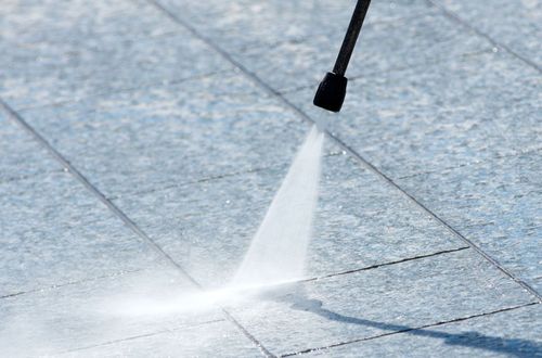 A person is using a high pressure washer to clean a tiled floor.