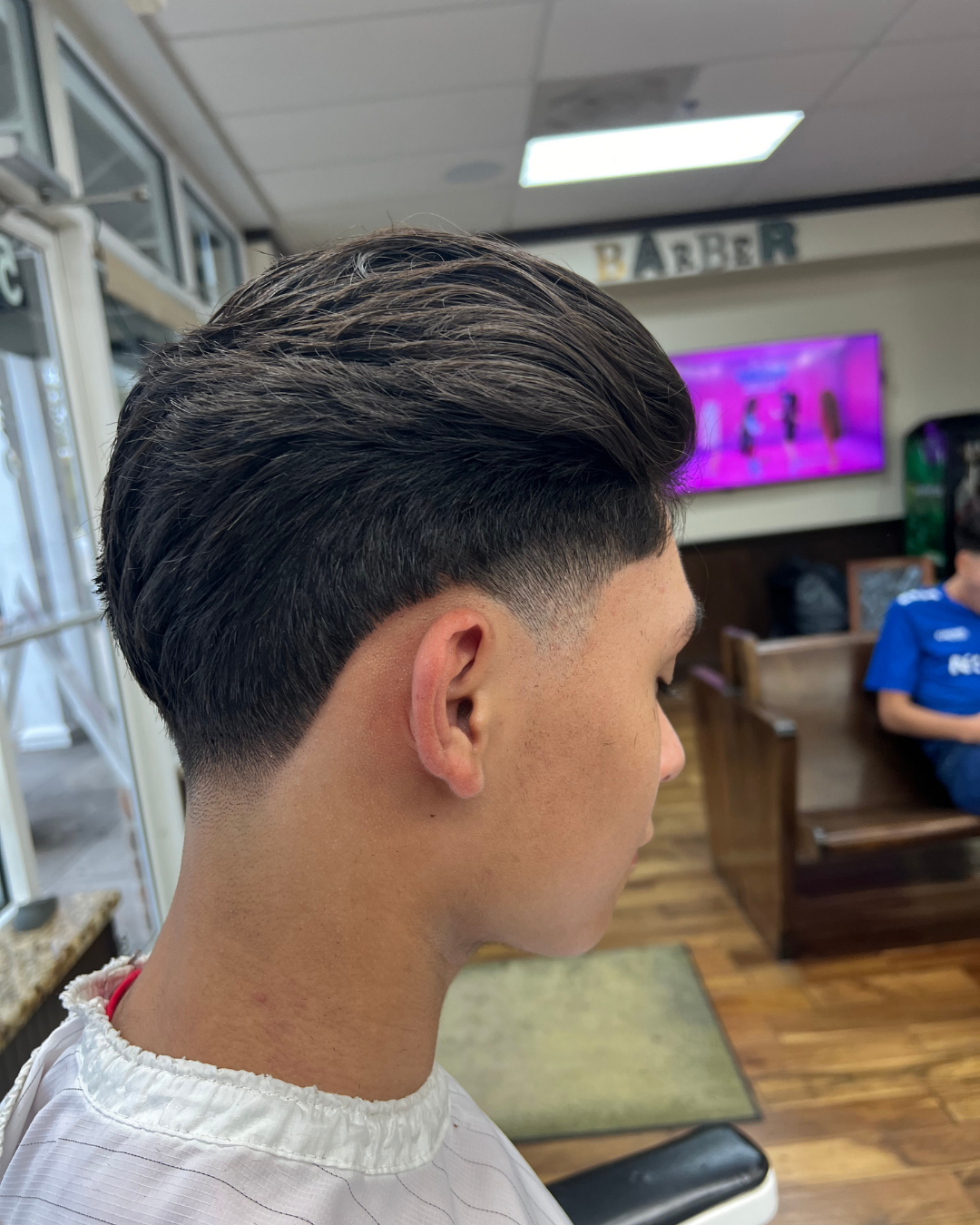 Person with dark hair and a faded haircut, sitting in a barbershop.