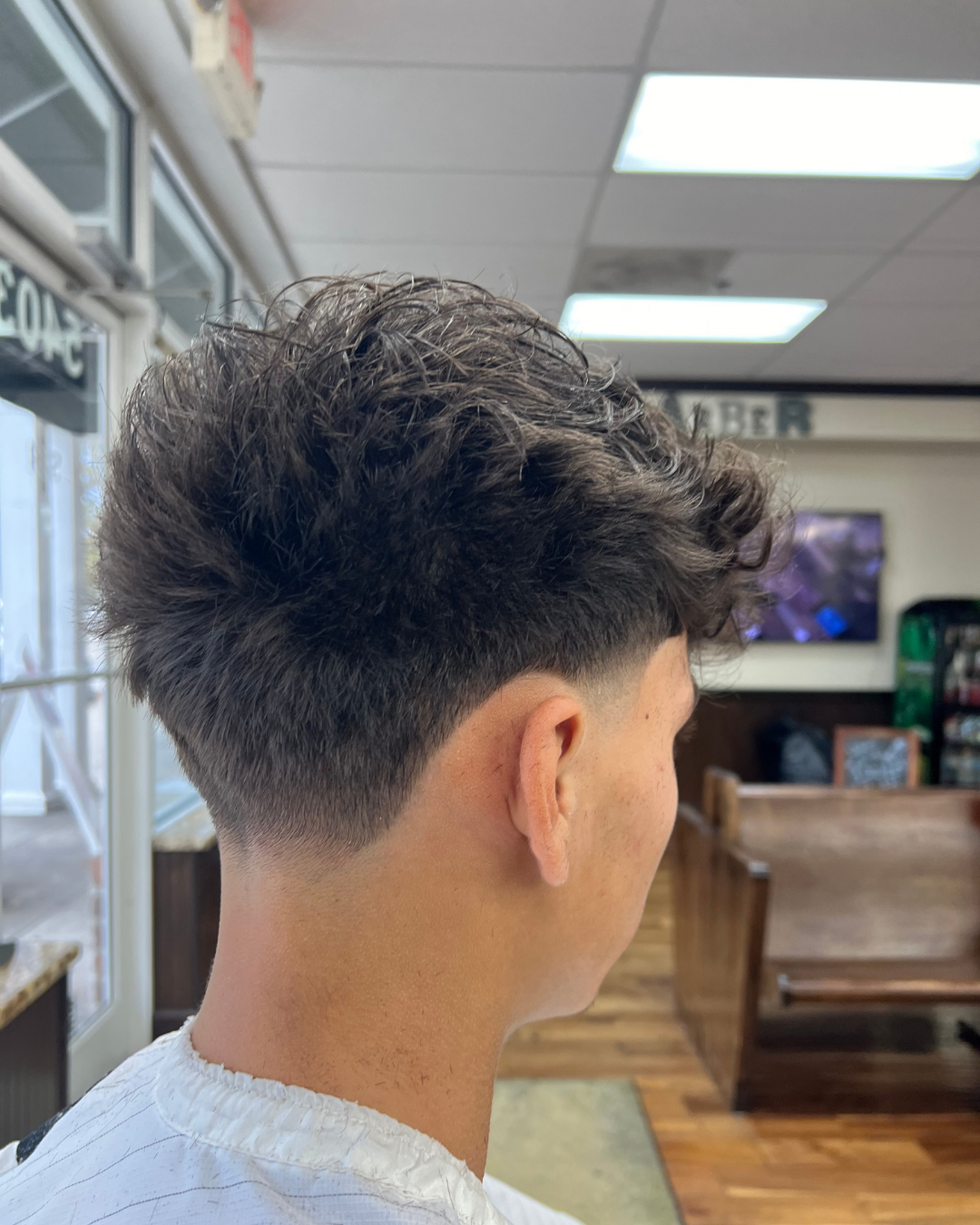 Man with faded haircut; dark hair on top, styled back. Shot from the back in a barbershop.