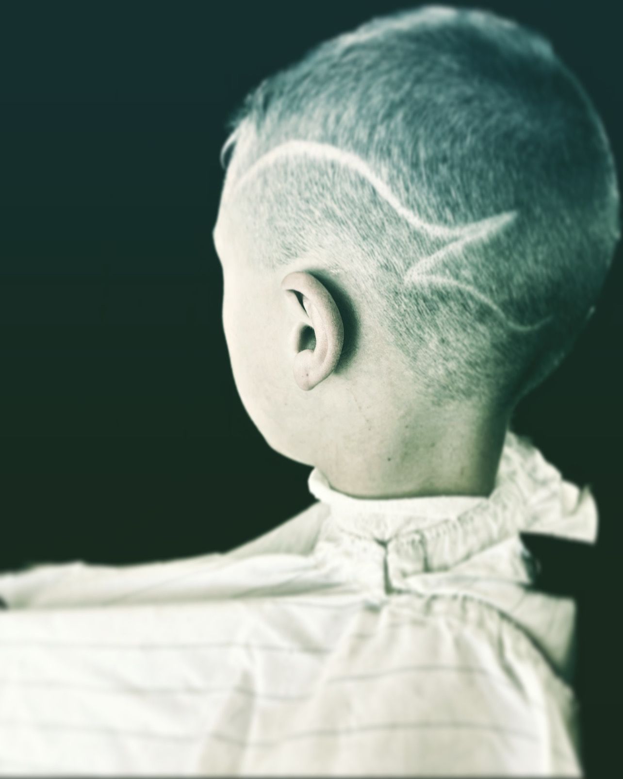 Boy with buzzcut hairstyle and patterned design shaved on the side, white shirt.