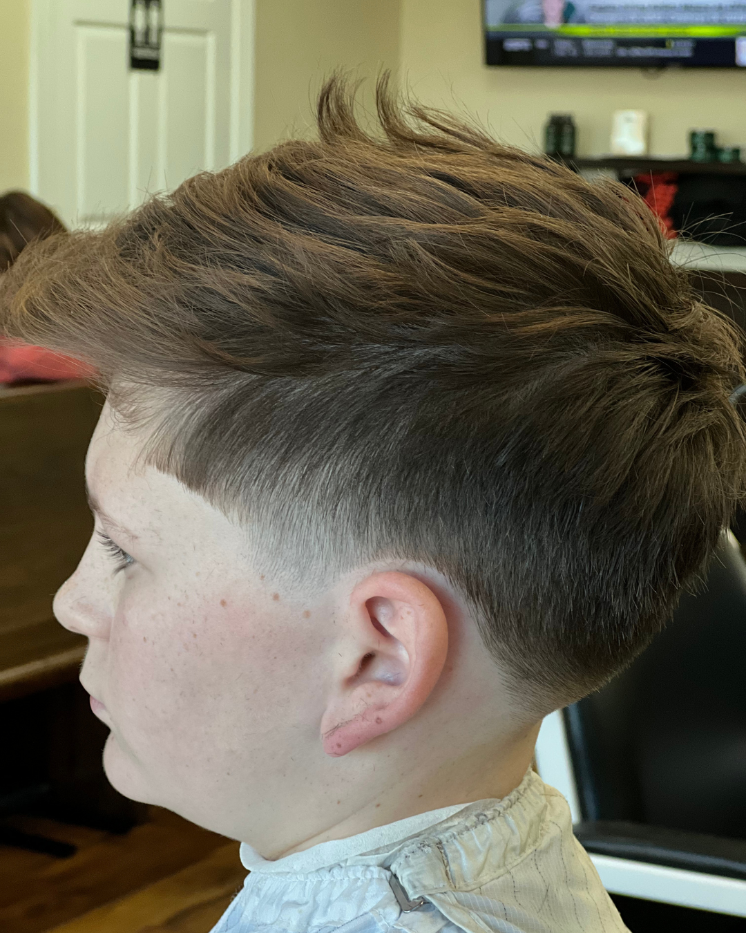 A person with a faded haircut, dark hair, and a high-volume top. The person is in a barbershop.