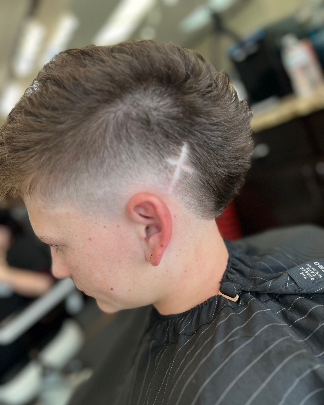 Boy with textured, faded mullet haircut, cross design shaved on side of head.