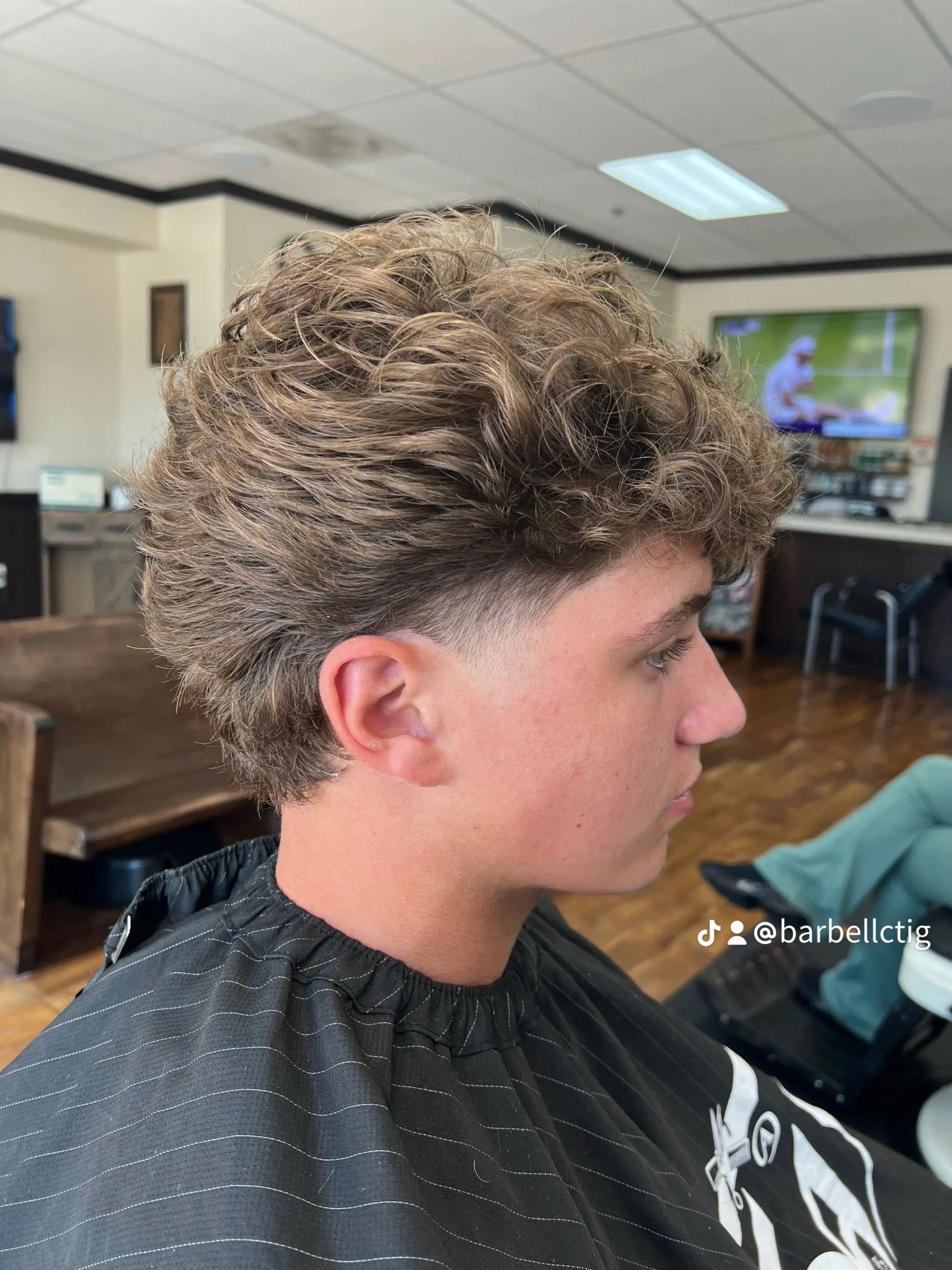 Man with curly hair and a tapered haircut in a barbershop setting.