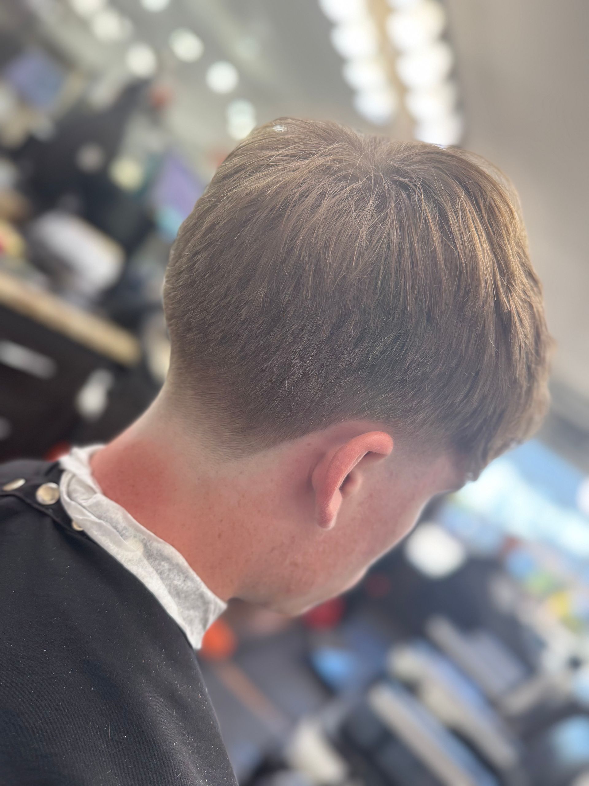 Person with a faded haircut, back facing the camera, in a barbershop.
