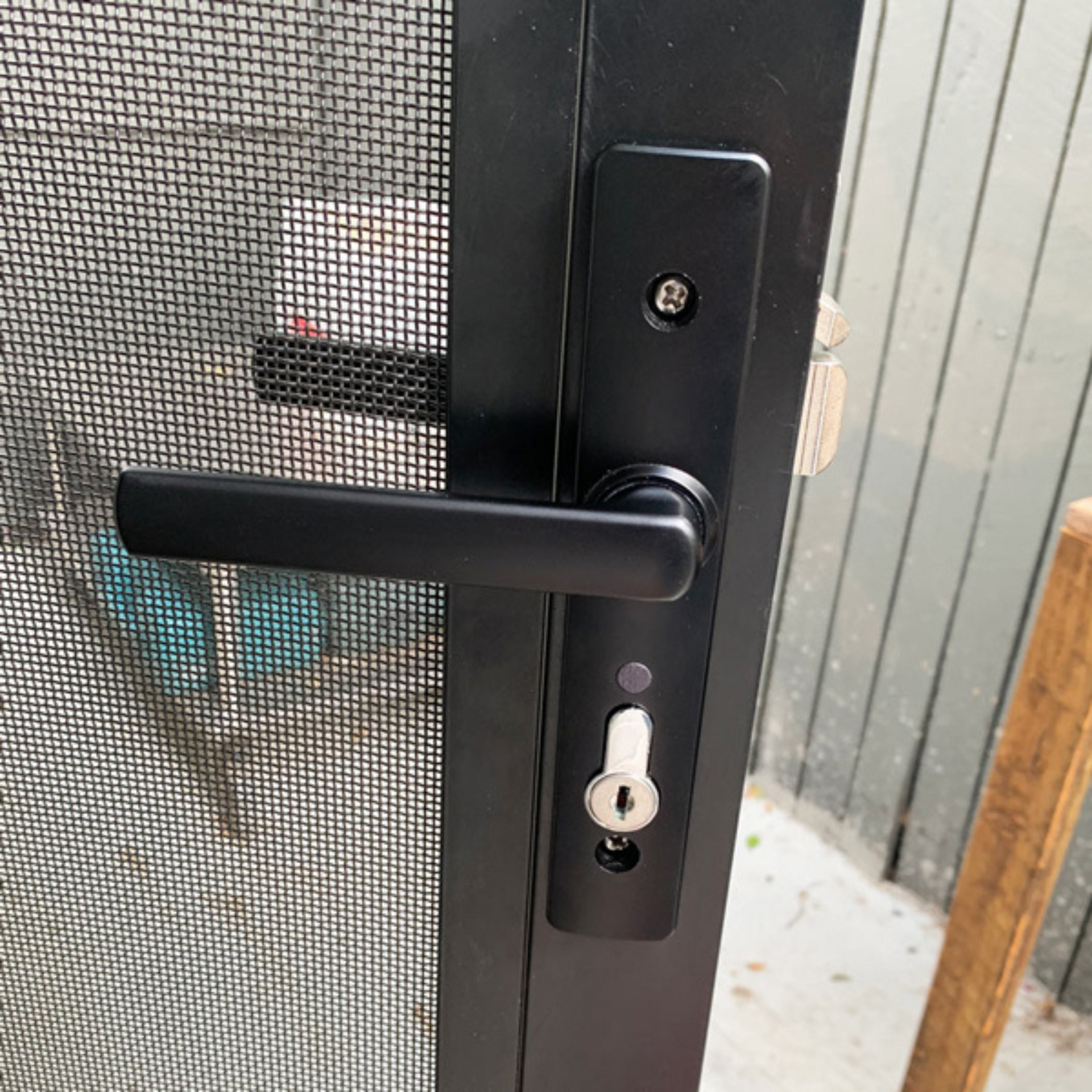 A close up of a black door handle on a screen door.