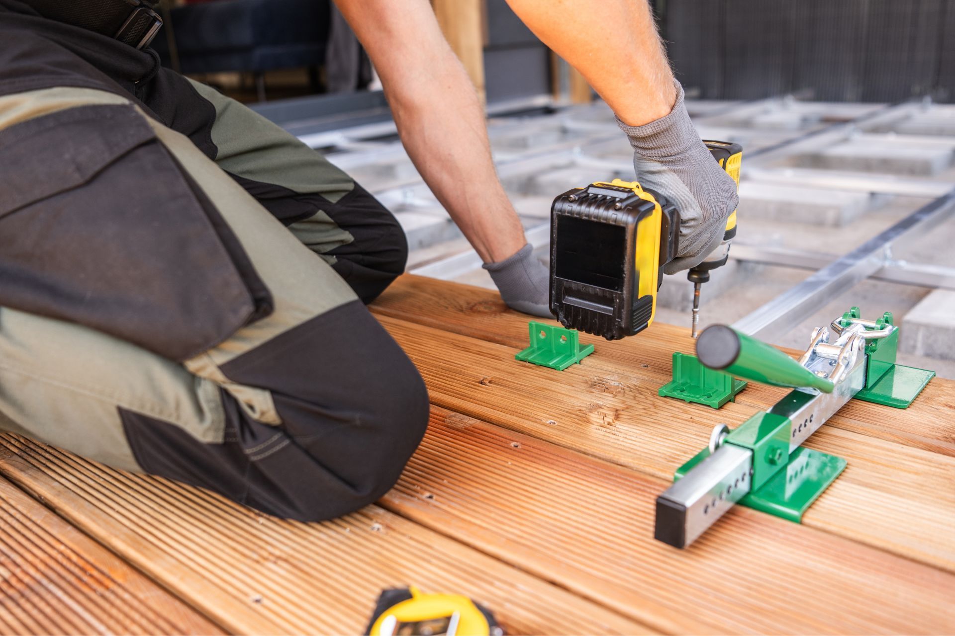 Person kneeling, using a drill to attach a wood deck board with leveling supports.