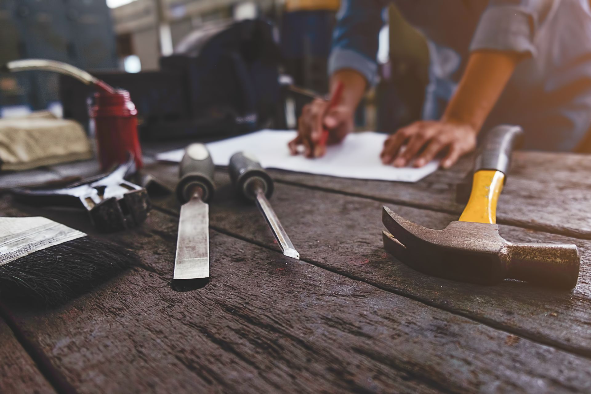 Tools on a wooden table with a person drawing on paper in the background.