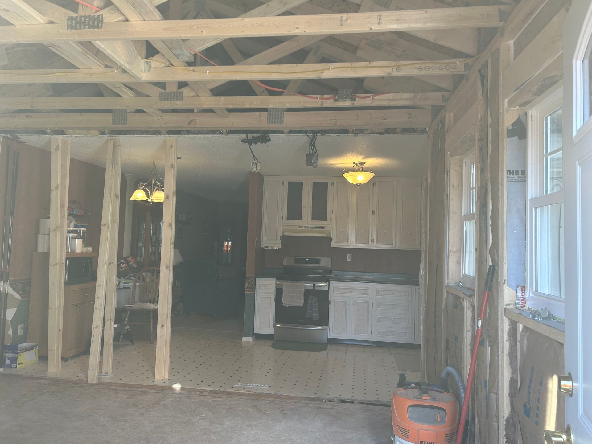 Construction site, partially framed interior with open view into a kitchen with white cabinets.