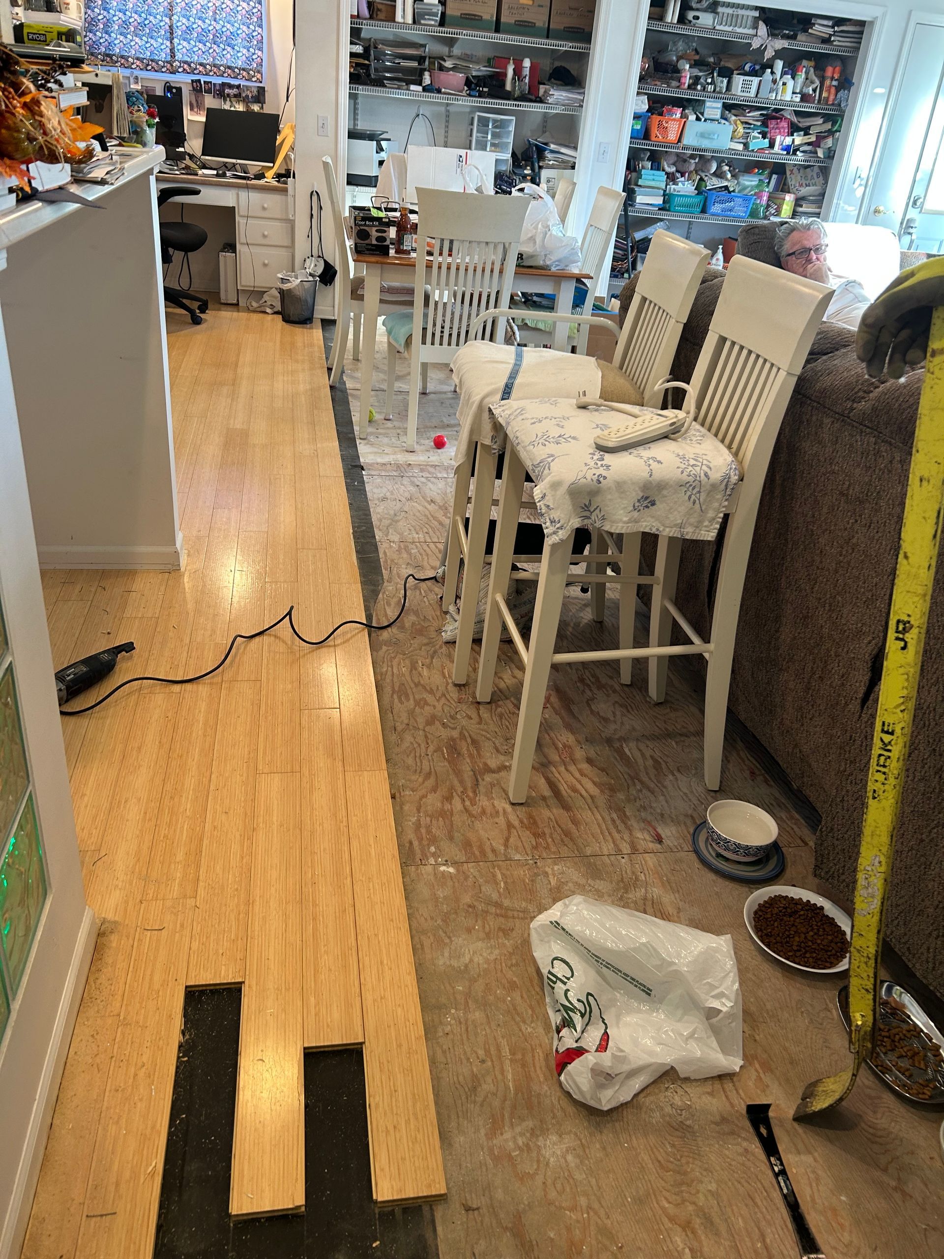 Flooring installation in a kitchen. Bamboo flooring partially installed with chairs and tools nearby.