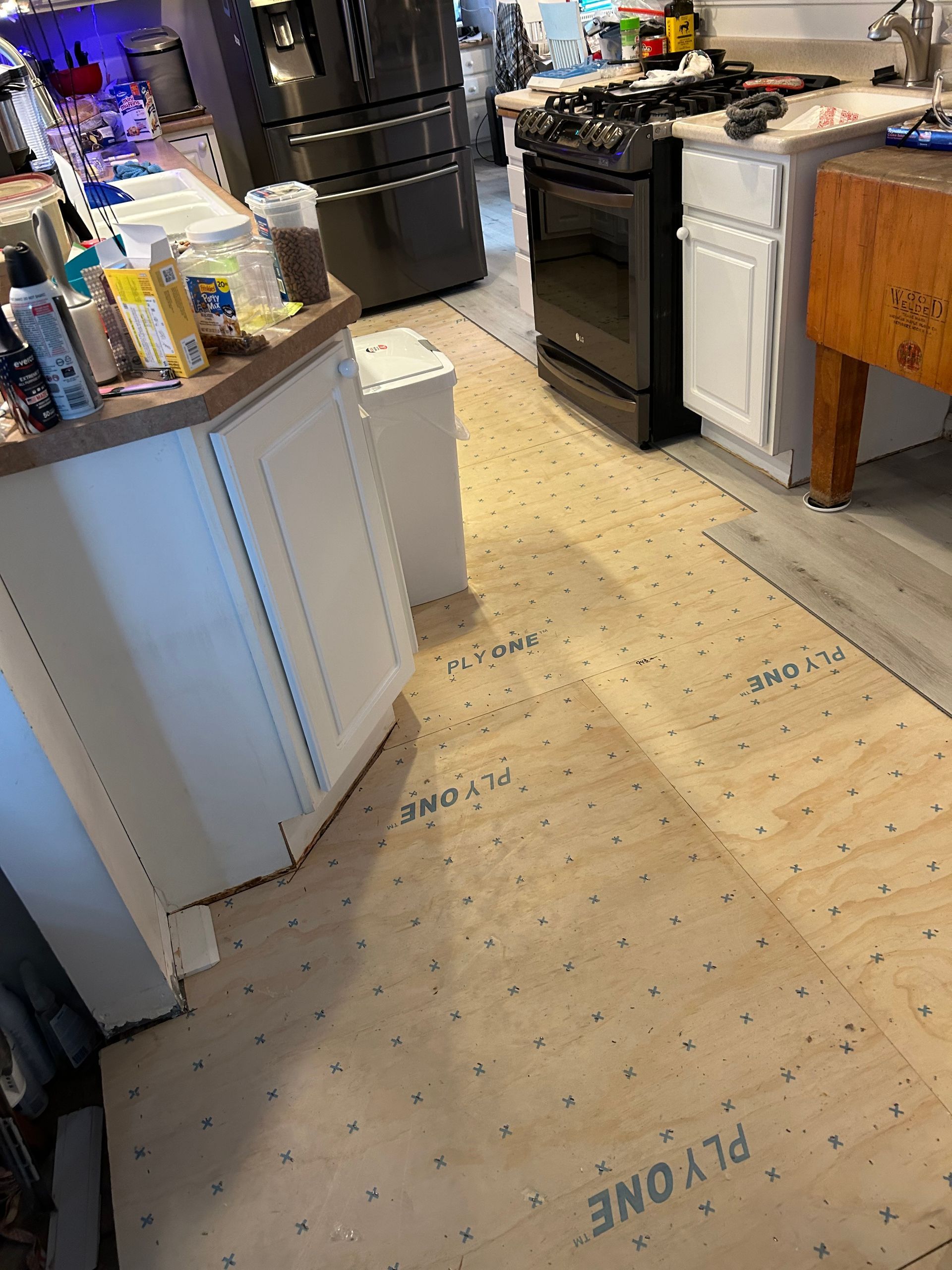 Kitchen renovation: new plywood subfloor installed. White cabinets, black stove, wood butcher block.
