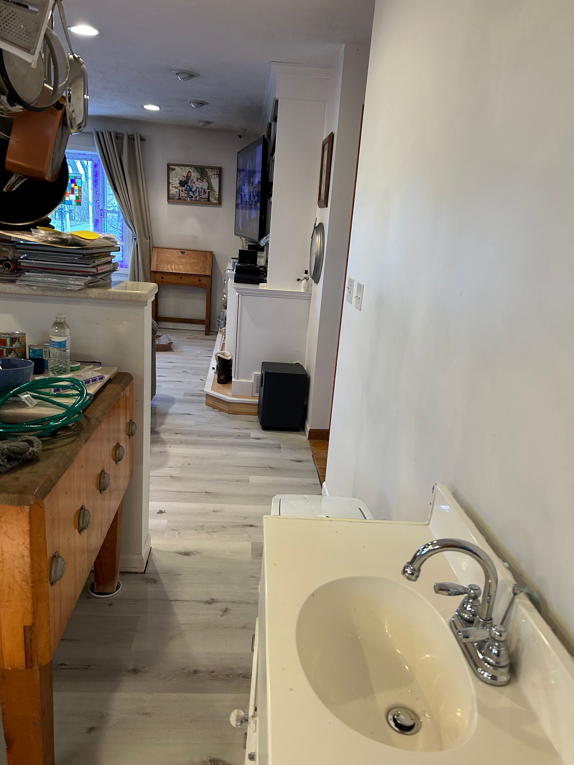 Bathroom with sink in the foreground, leading into a hallway and adjacent living space.