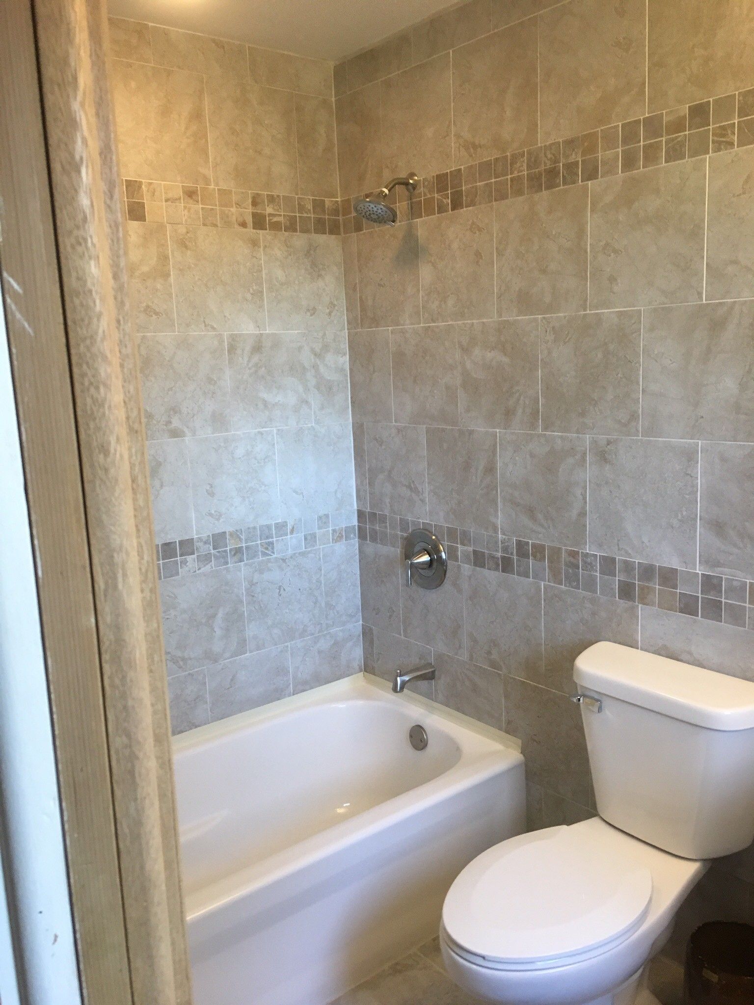 Bathroom with a white bathtub and toilet. Beige tile walls with a decorative border.