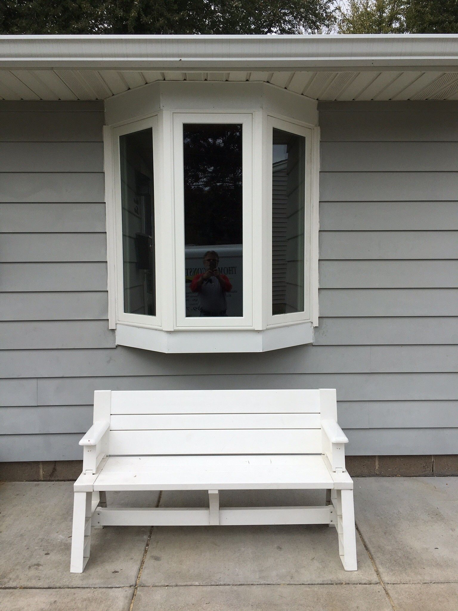 White bench under a bay window on a gray house exterior.
