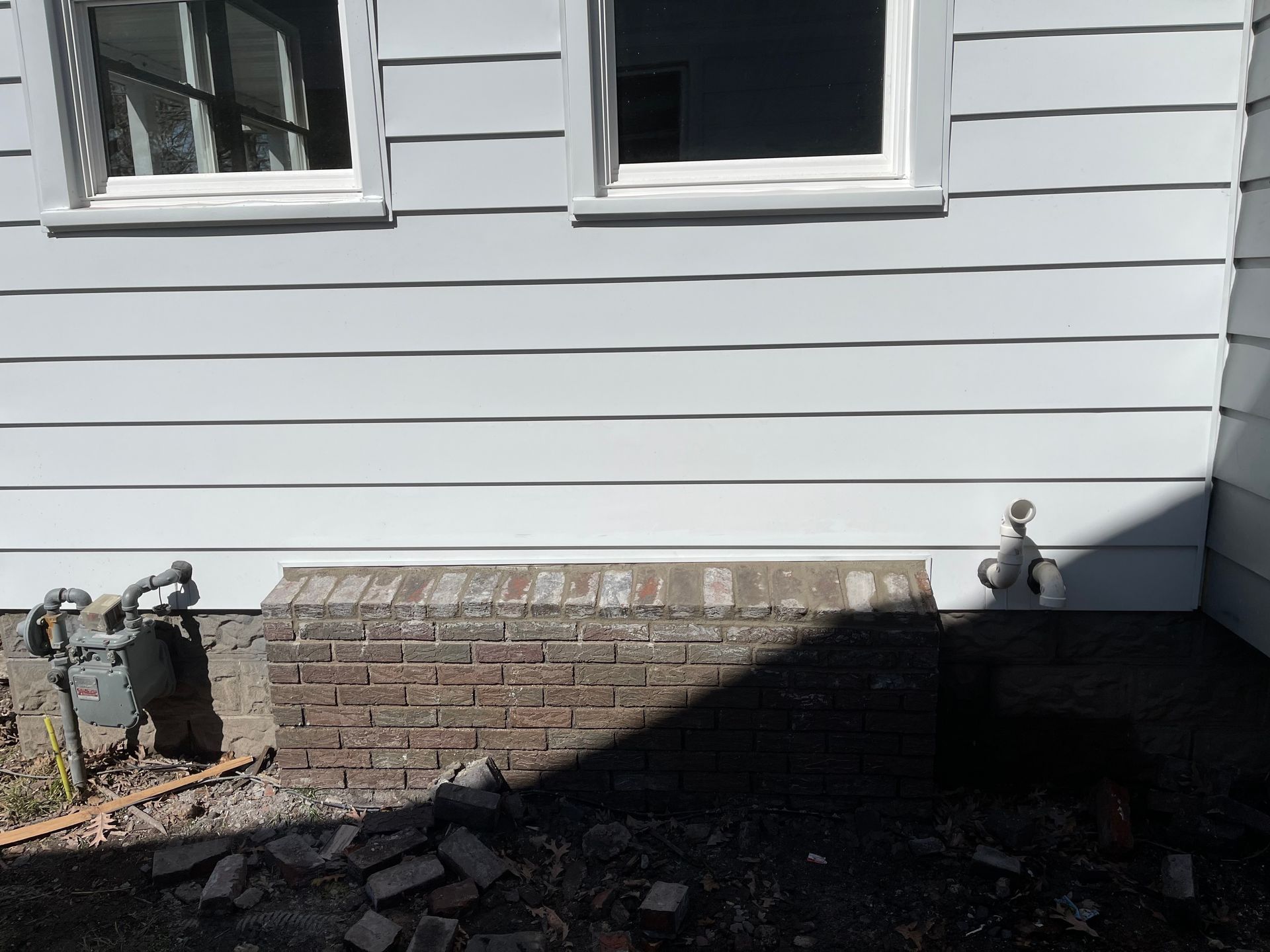 Exterior wall with two windows above a brick foundation, gas meter, and water spigot.