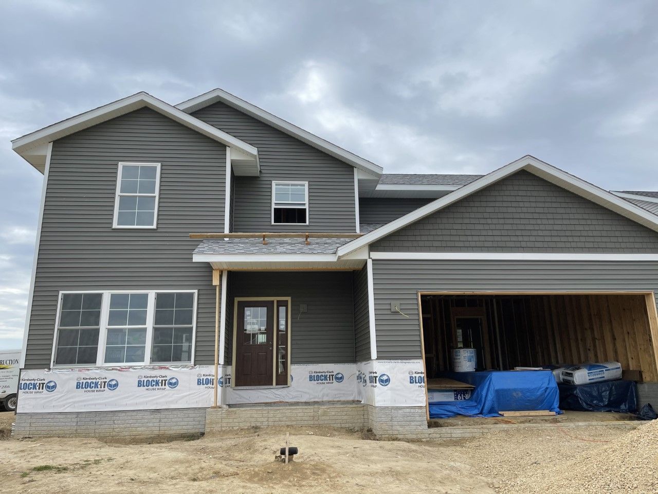Two-story house under construction with gray siding and unfinished garage. Overcast sky.