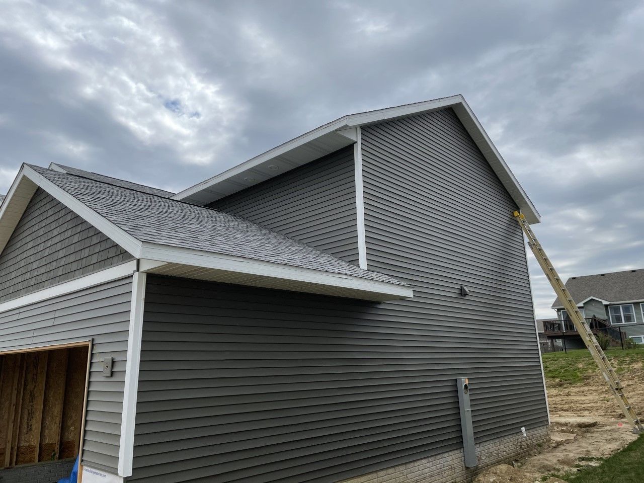 Exterior view of a partially built gray house with a ladder leaning against the side. Overcast sky.