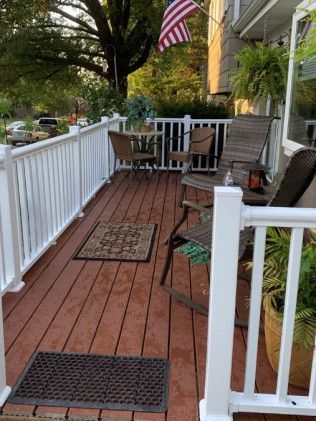 Wooden porch with white railing, chairs, table, and American flag.