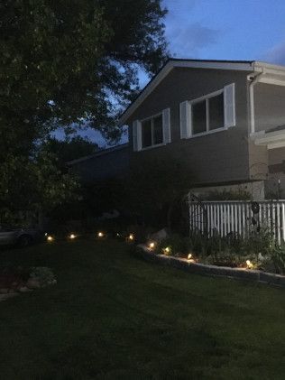 Night view of house with path lit by small lights along a dark grassy yard.