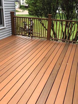 Wooden deck with brown railing; house siding on left, green foliage in the background.