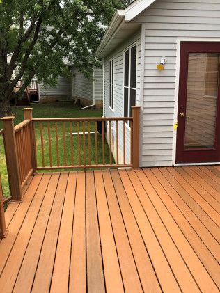 Wooden deck with railing, connected to a light gray house with a burgundy door.