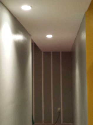 Narrow hallway with recessed ceiling lights and partially finished walls.