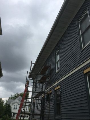 Scaffolding set up beside a building with dark blue siding, under a cloudy sky.