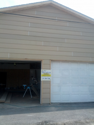 Tan garage with white garage door and open bay, sign on the side.