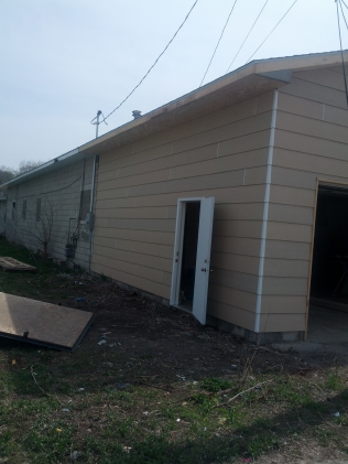 Beige building with a detached white door leaning against the wall, near an open garage.