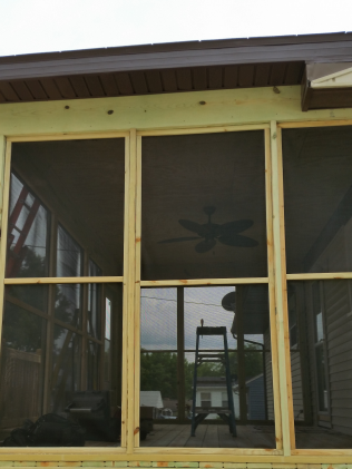 Screened porch under construction, showcasing wooden frames with installed screens; ladder visible inside.