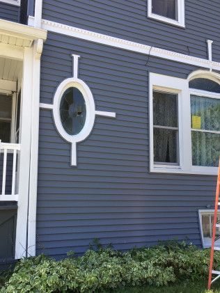Gray clapboard siding on a house with an oval window and white trim.