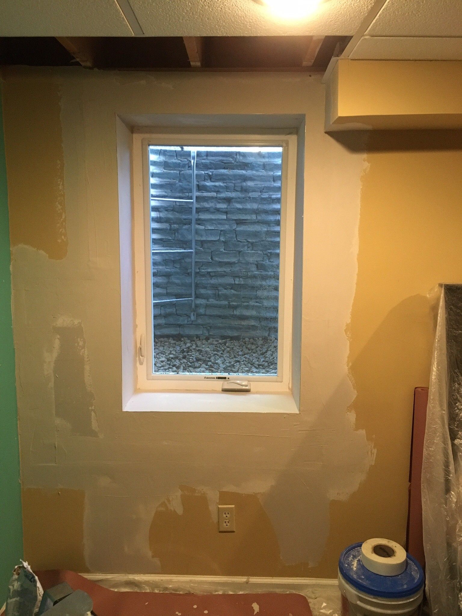 Basement window with concrete brick well, partially finished walls, and a bucket on the floor.