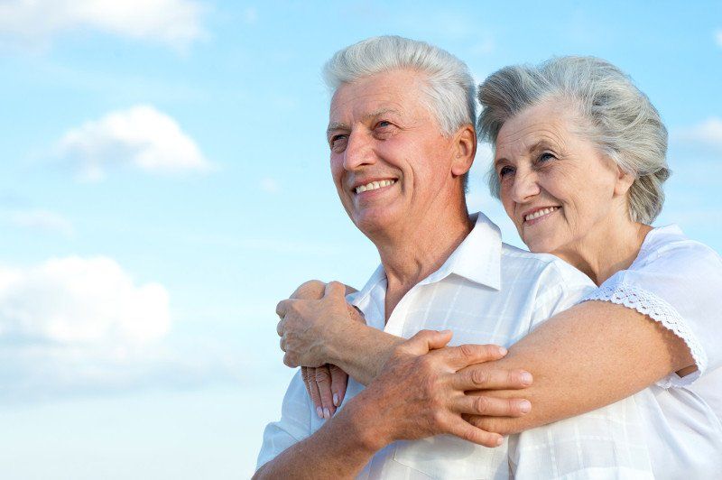 Elderly couple smiling under blue sky with minimal clouds