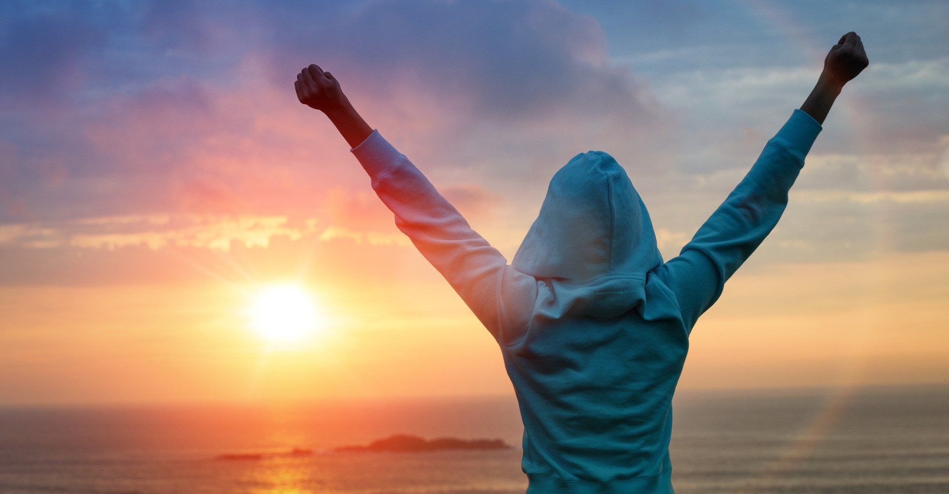 lady in a hooded top looking across the ocean as the sun sets