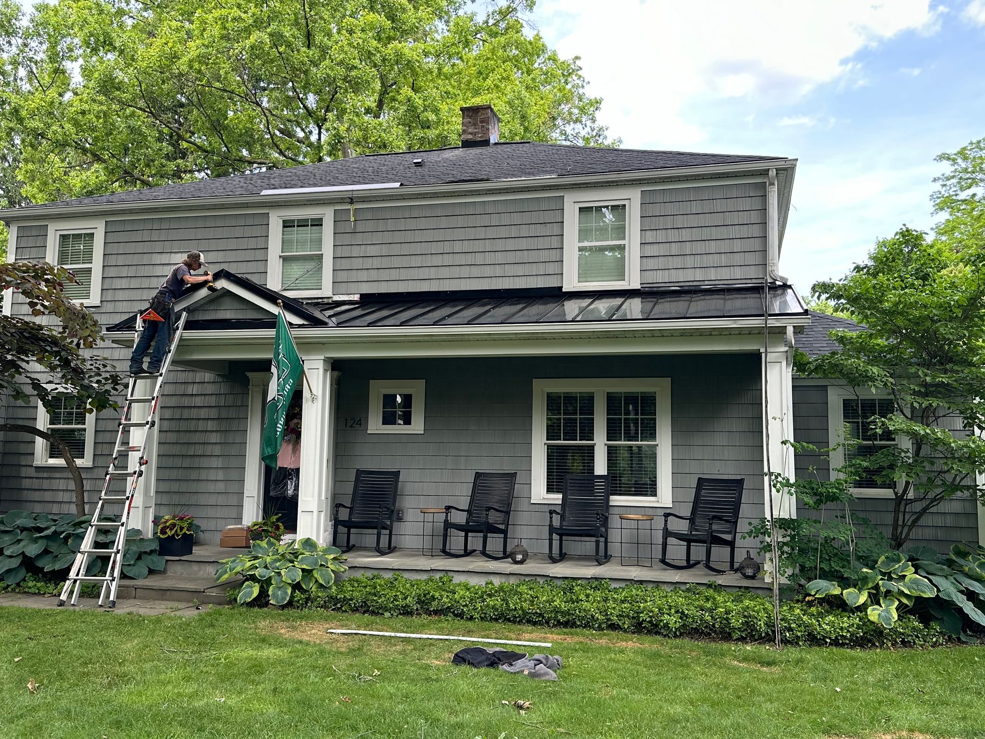 A man is standing on a ladder painting the roof of a house.