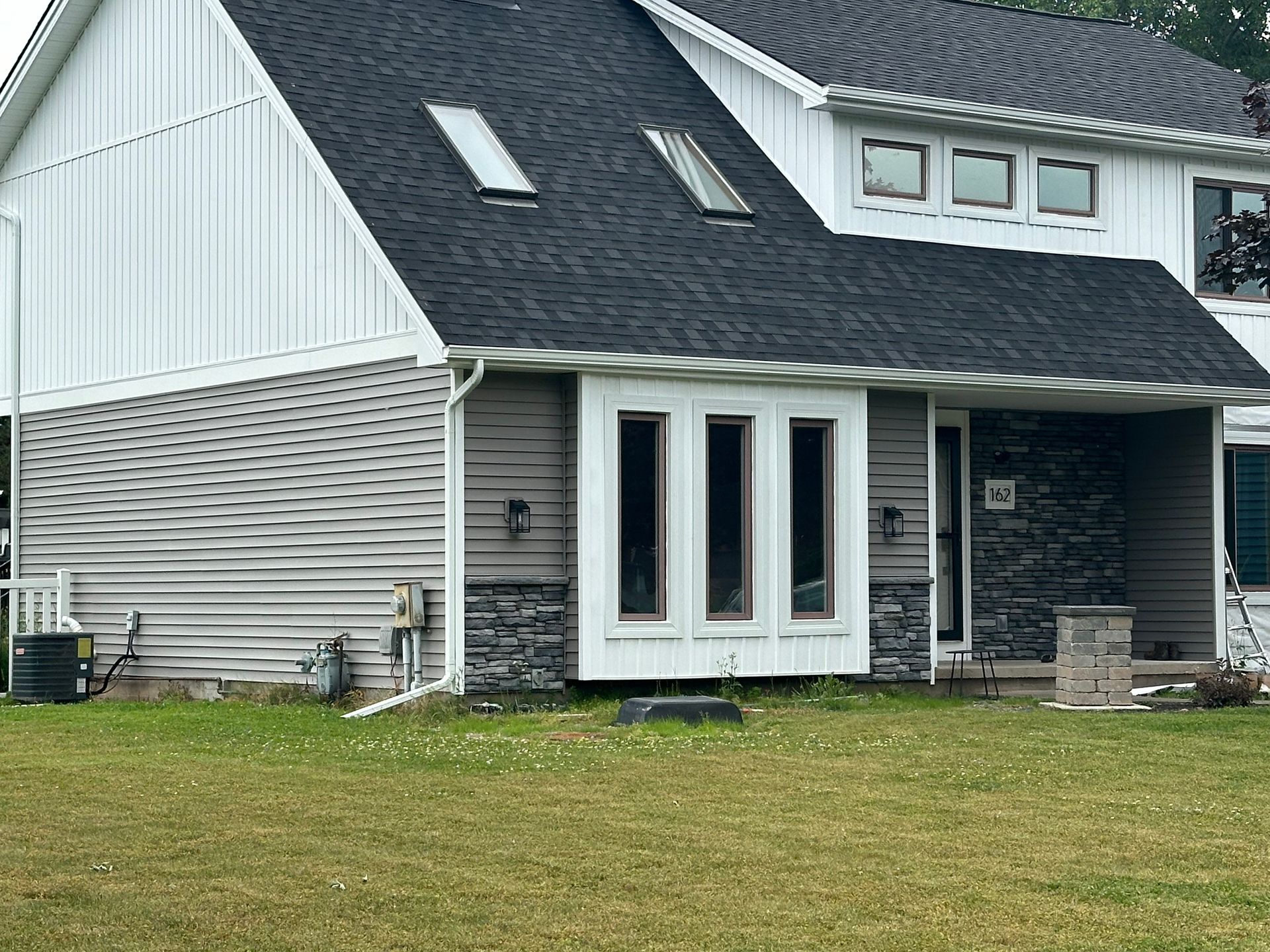 A large white house with a black roof is sitting on top of a lush green field.