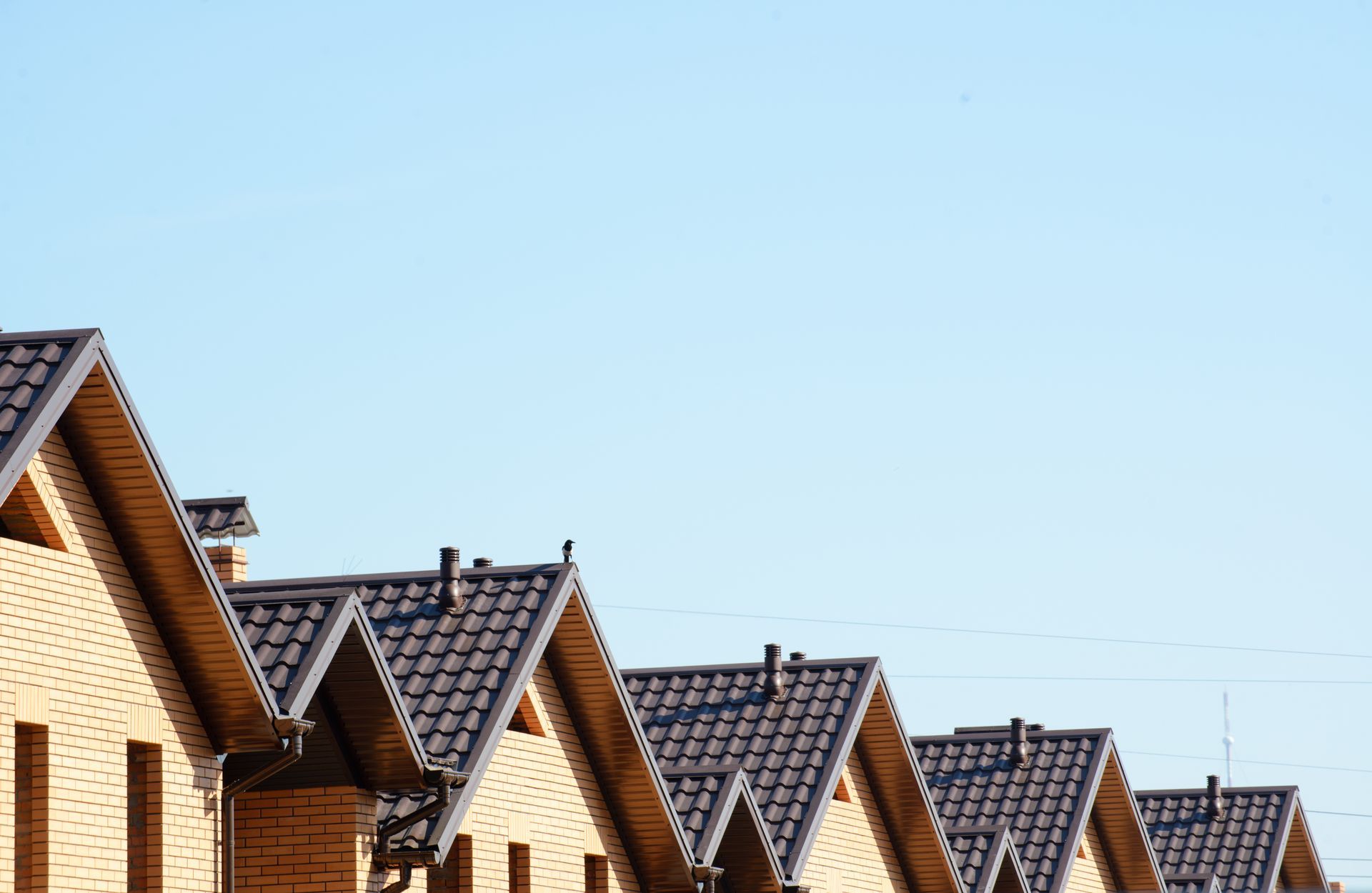 Row of brick houses with brown roofs against a clear blue sky.