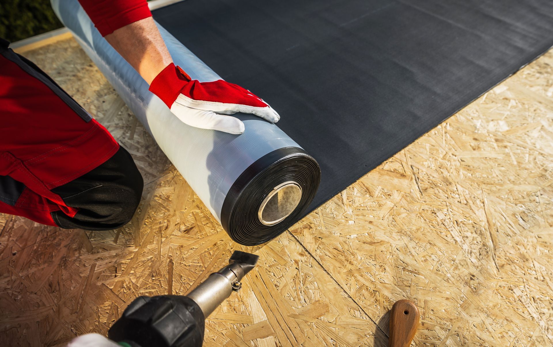 A man is laying a roll of roofing material on a roof.