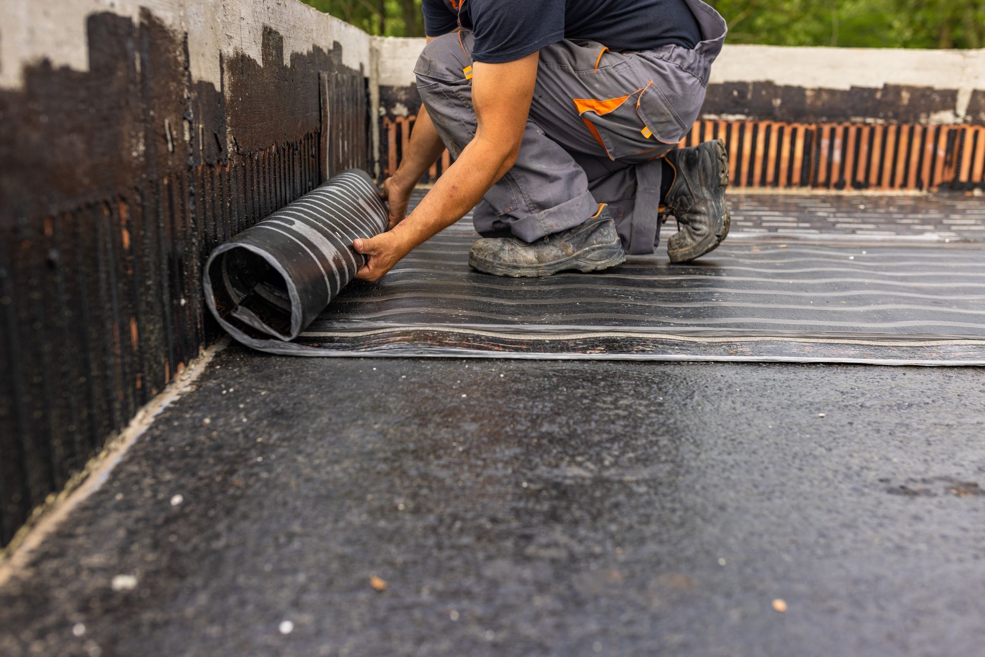 A man is laying a roll of asphalt on a roof.
