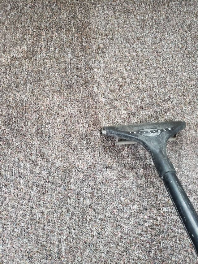A vacuum cleaner is cleaning a brown carpet.