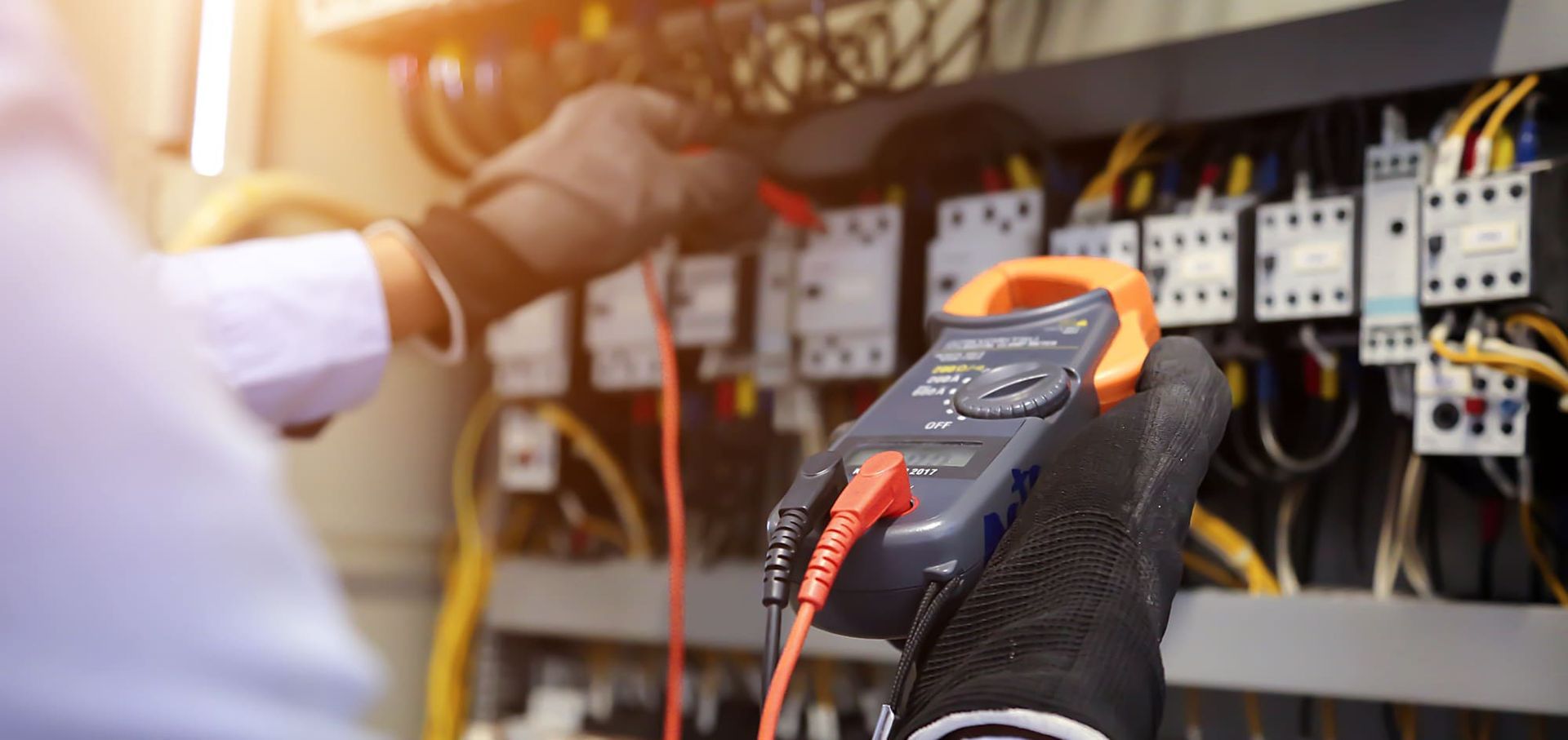 An electrician is using a clamp meter to test a circuit board.