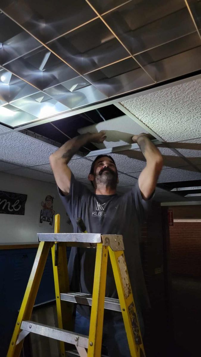 A man is standing on a ladder working on the ceiling