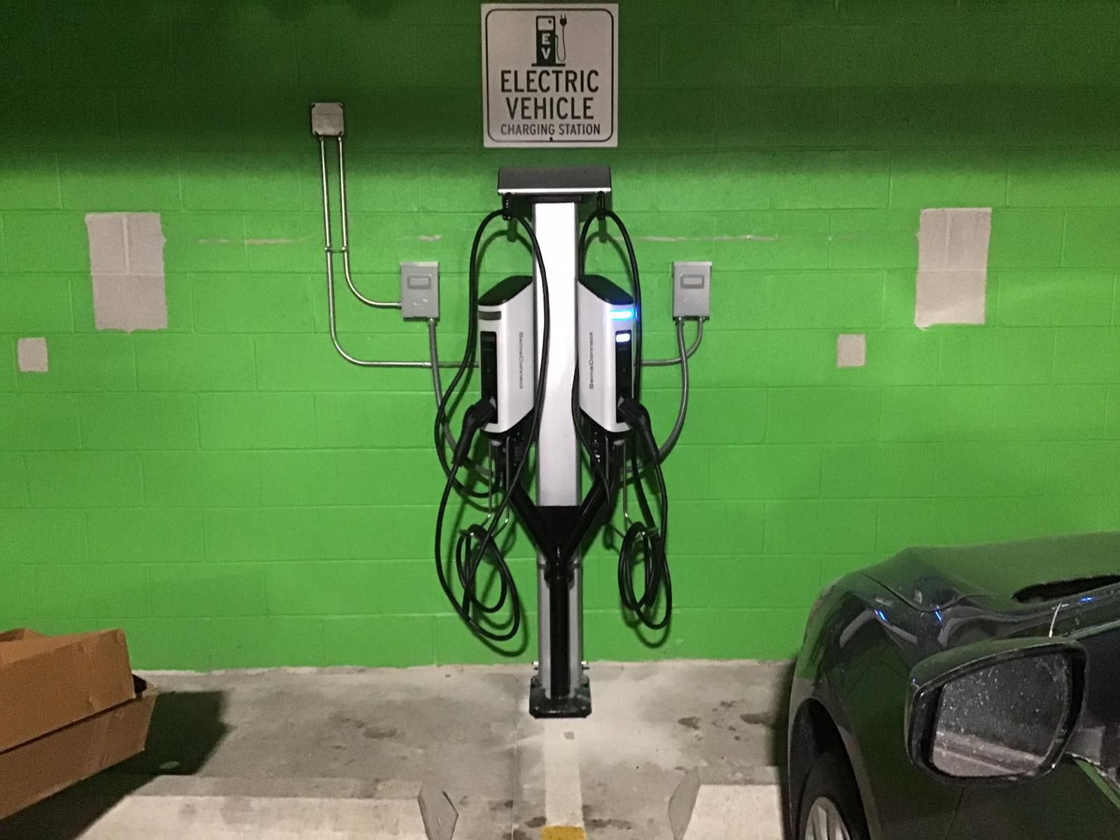 A car is parked next to a charging station in a parking garage.