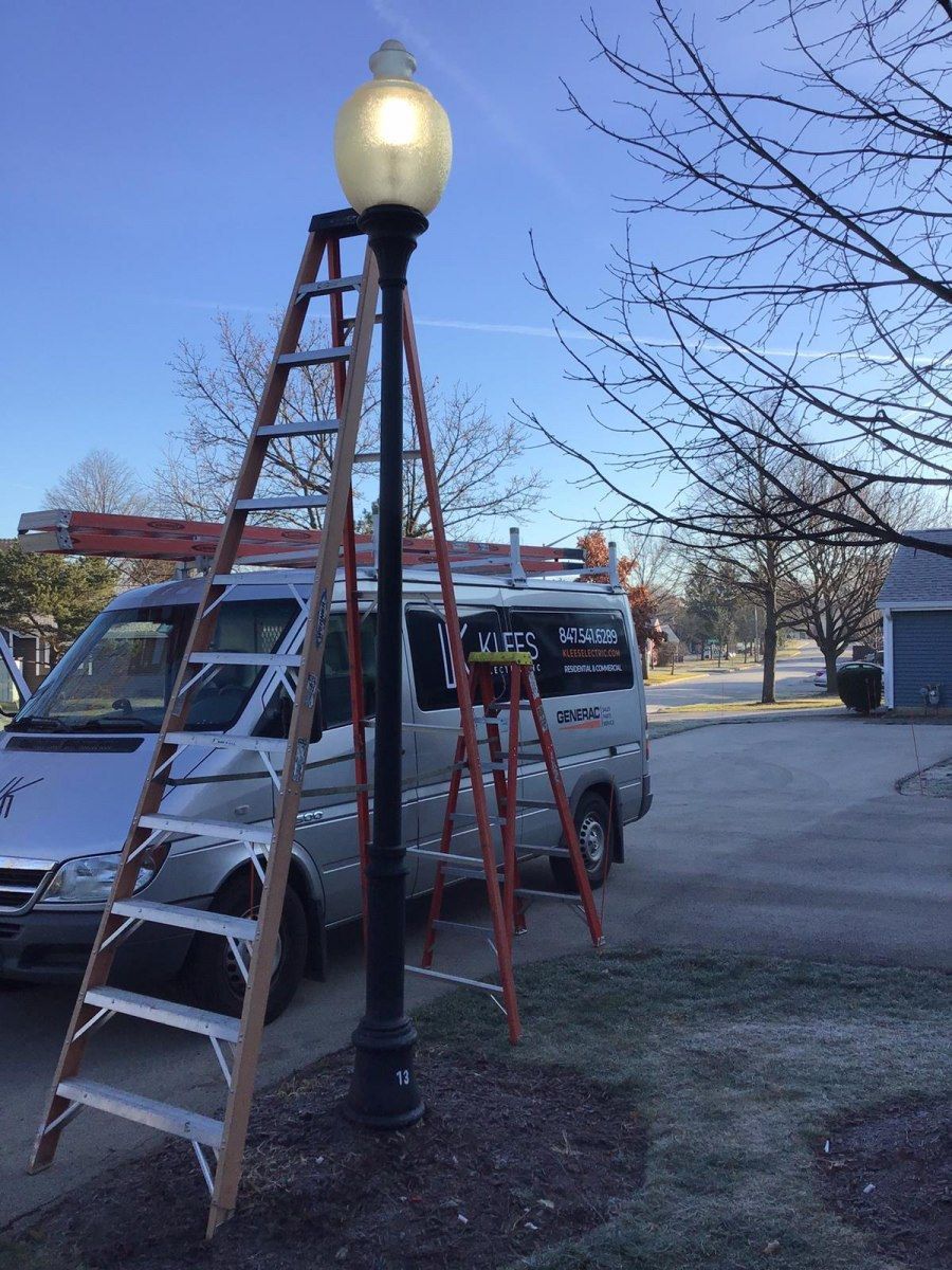 A ladder is sitting on top of a street light next to a Klees electric inc van.
