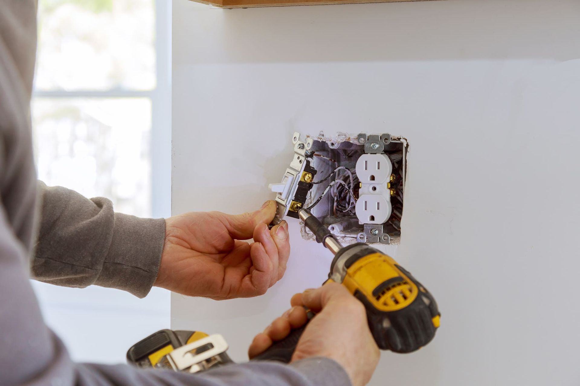 A man is installing an electrical outlet on a wall with a drill.