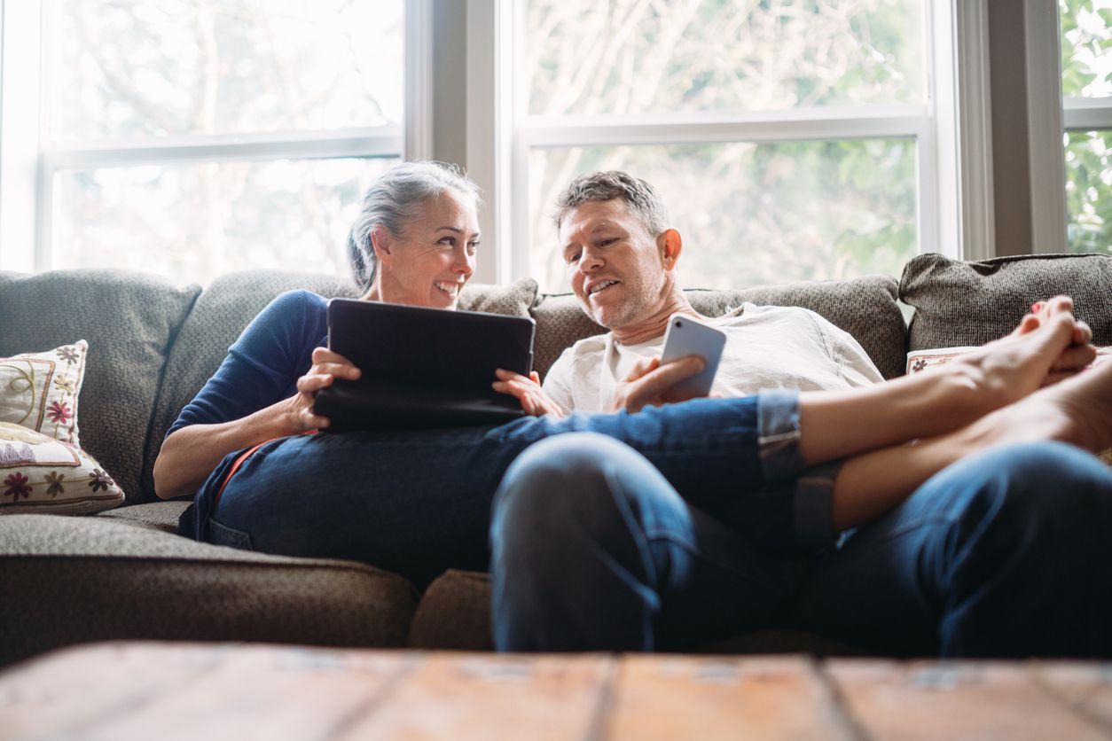 A man and a woman are sitting on a couch looking at a tablet.