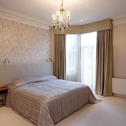 Bedroom with bed, patterned wallpaper, window with curtains, and chandelier.