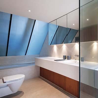 Modern bathroom with toilet, floating sink, wood cabinet, large mirror, and blue-tinted slanted window.