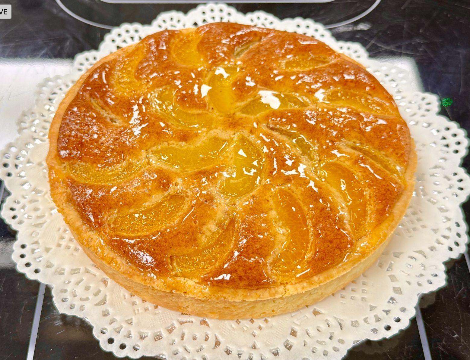 Peach tart on a white doily, with glazed fruit arranged in a spiral pattern.