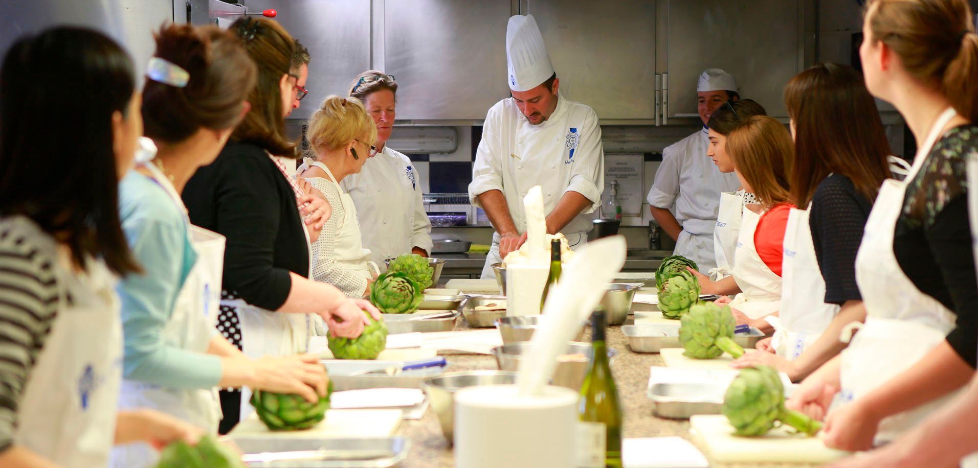 Chef demonstrating food prep to students in a kitchen setting. Students wear aprons and prepare artichokes.