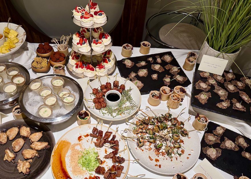 Buffet table with various appetizers, desserts, and a tiered cake.